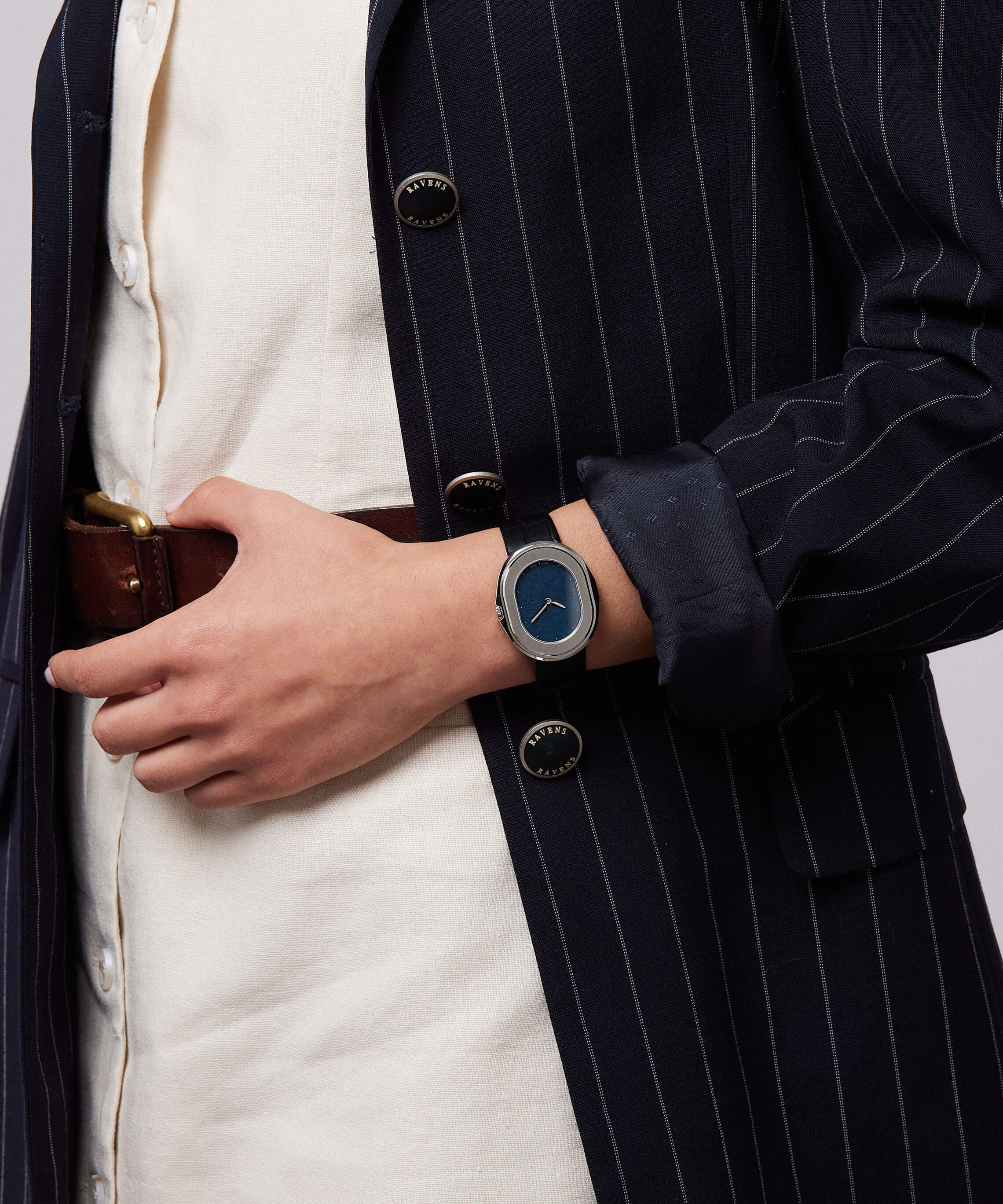Serica Watches - Gros plan sur femme tenant ceinture avec SERICA 1174-4 cadran lin bleu automatique. Veste rayé et robe blanche.