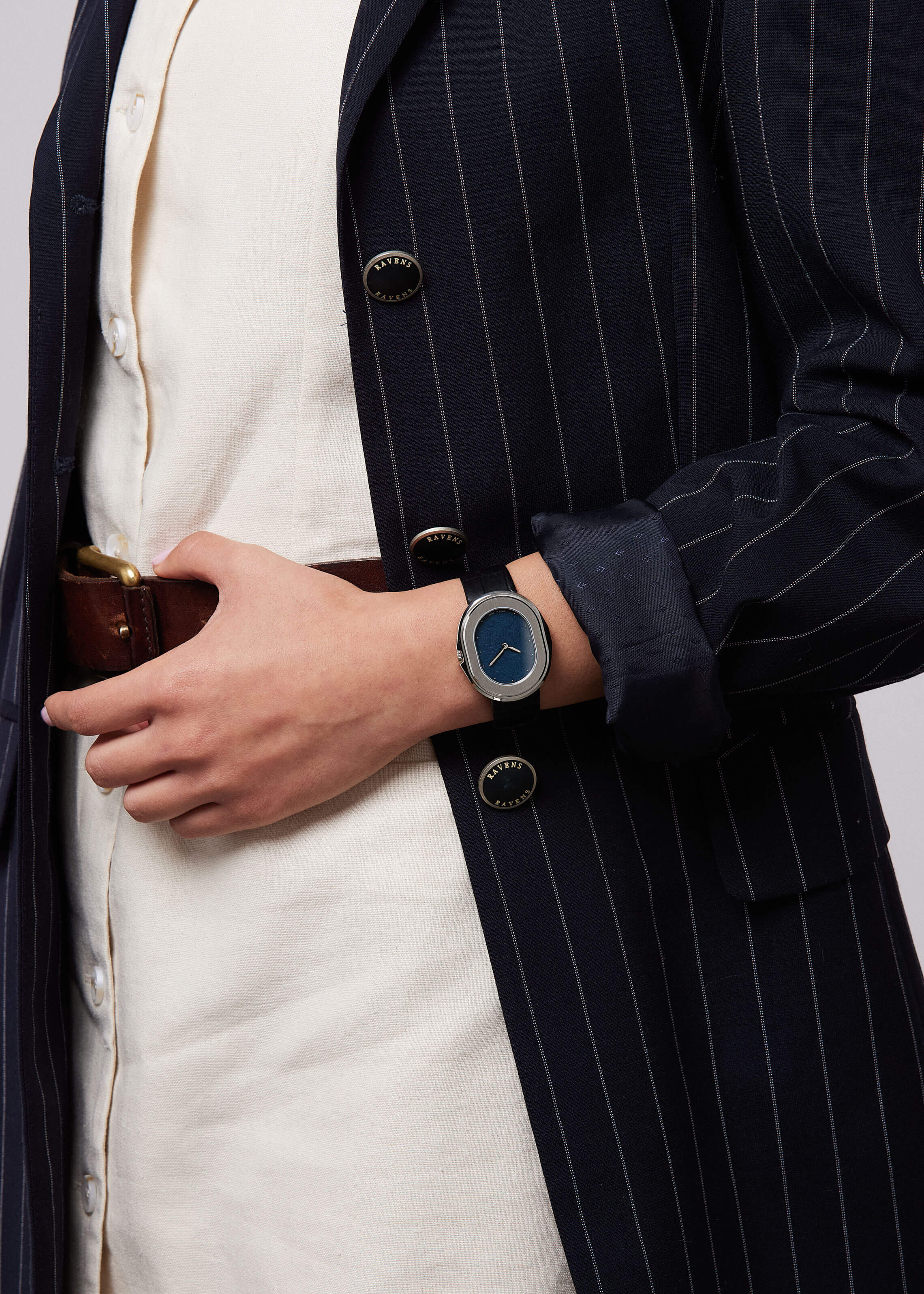 Serica Watches - Gros plan sur femme tenant ceinture avec SERICA 1174-4 cadran lin bleu automatique. Veste rayé et robe blanche.